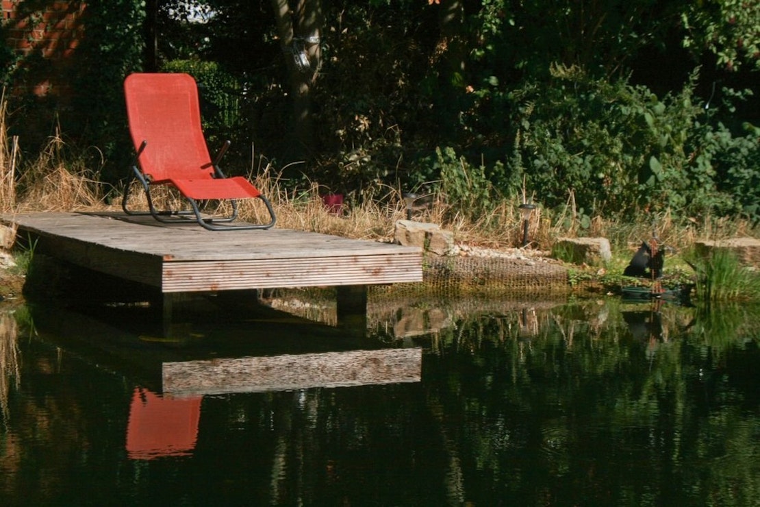 Roter Liegestuhl auf dem Holzsteg über dem Teich