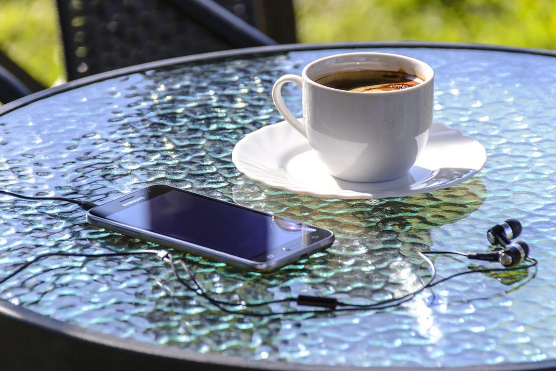 Glastisch auf der Terrasse mit einem Handy und einer Tasse Kaffee