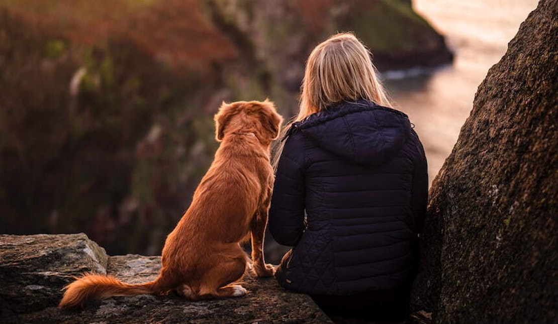 Ein Frau sitzt neben ihrem Hund und blickt in die Ferne