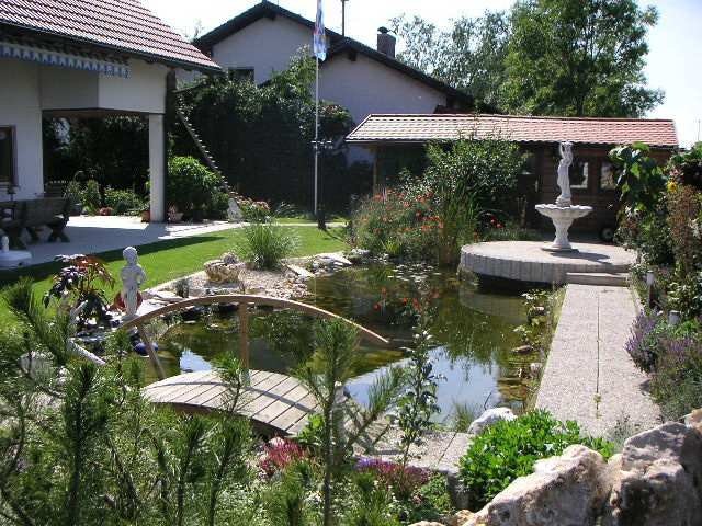 Teich im gepflegten Garten mit Brücke und Statue