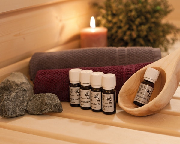 Ätherische Öle für die Sauna mit einer hölzernen Schöpfkelle und Handtüchern, sowie einer Kerze im Hintergrund