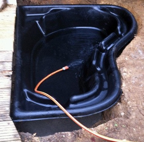 Teichschale aus PE wird mit einem Gartenschlauch mit Wasser gefüllt.