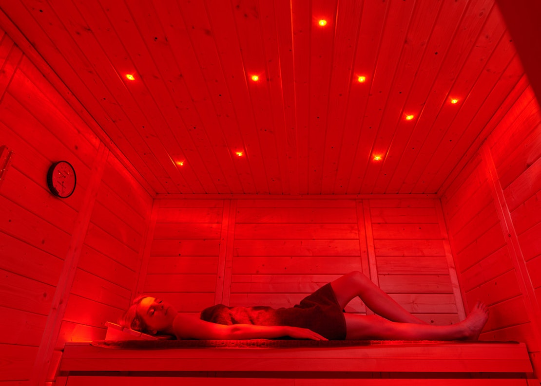 Eine Frau entspannt auf einer Saunabank mit rotem Licht und Sternenbeleuchtung