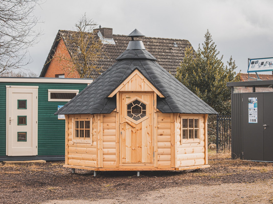 Grillkota und Gartenhäuser Ein Holzgartenholz mit grünem Farbanstrich steht neben einer Grillkota aus Holz und einem Gerätehaus aus Metall