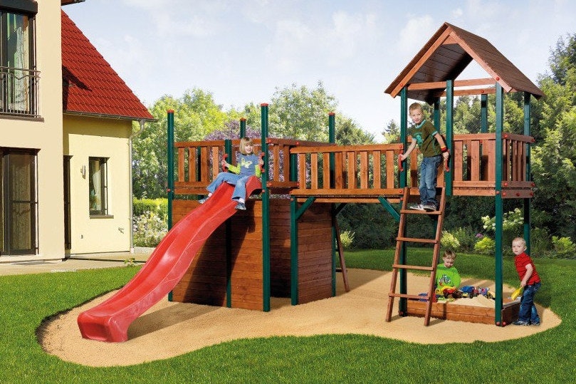 Vier Kinder vergnügen sich mit einem Spielturm mit Leiter, Rutsche und Sandkastenim Garten
