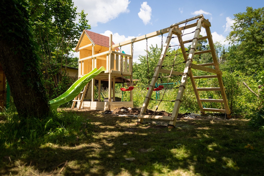Ein Kinderspielgerät mit Haus, Klettergerüst und Rutsche in einem sonnigen Garten